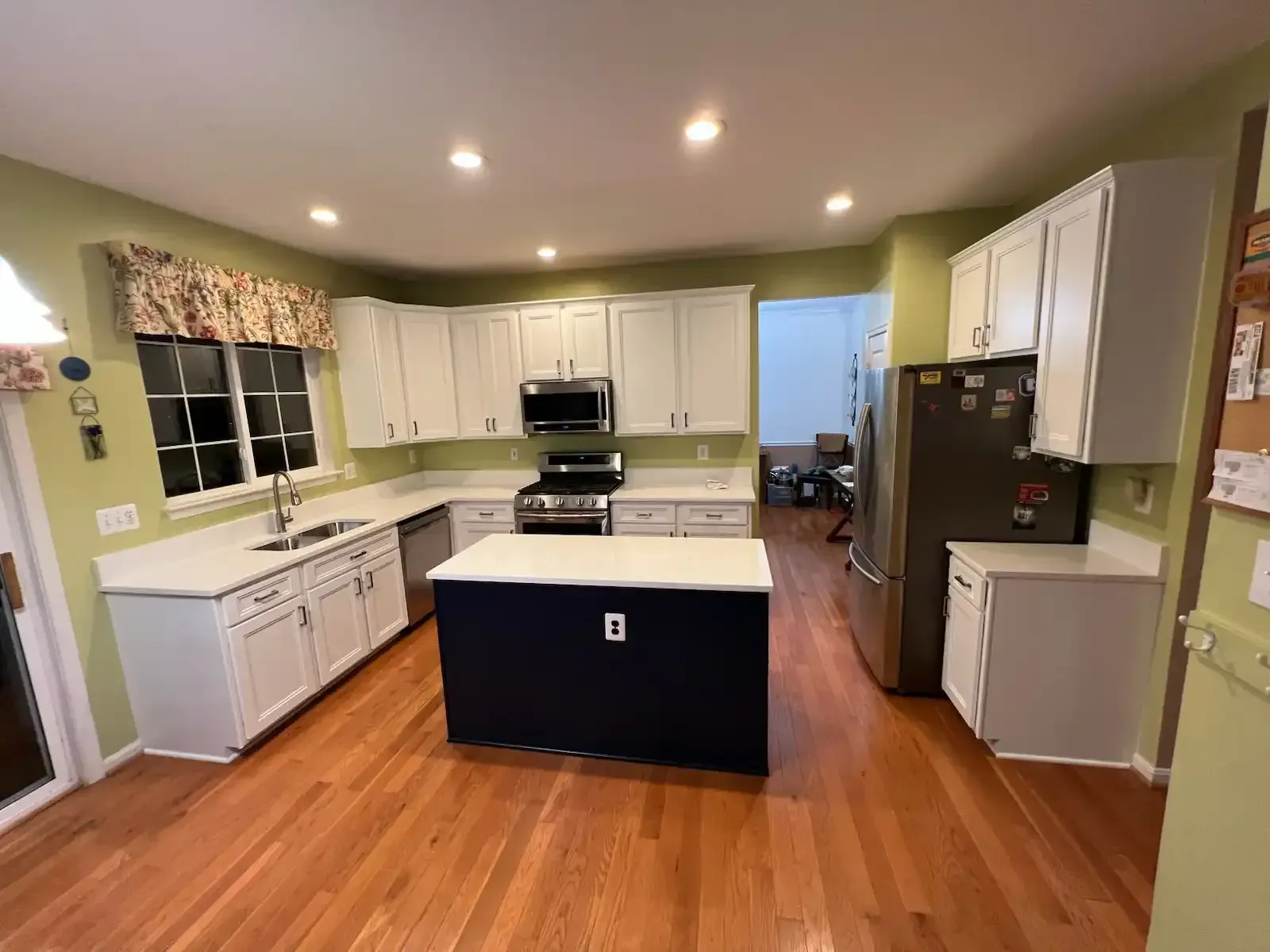 Bright kitchen with white cabinets, black island, wood floors, and green walls.