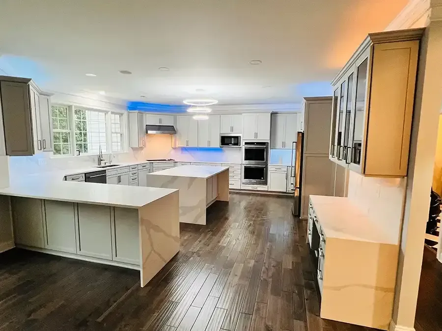 Bright, modern kitchen with white cabinets, dark wood floors, and a large island under warm ceiling lights.