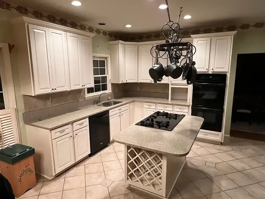 Modern kitchen with white cabinets, granite island, hanging pot rack, and tan tile floor