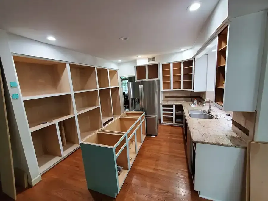 Unfinished kitchen with bare wood cabinets, white countertops, and hardwood floor under renovation.