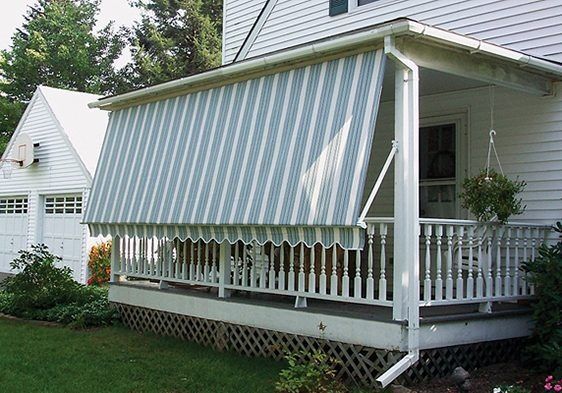 White house porch with striped green-and-white awning and railing, beside a grassy yard