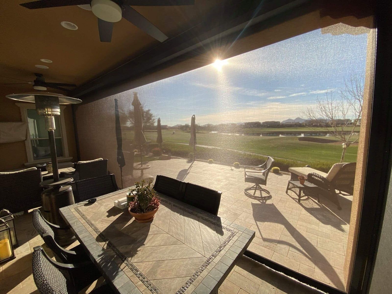 Sunlit patio with table, chairs, and a view of green fields through a large glass window.