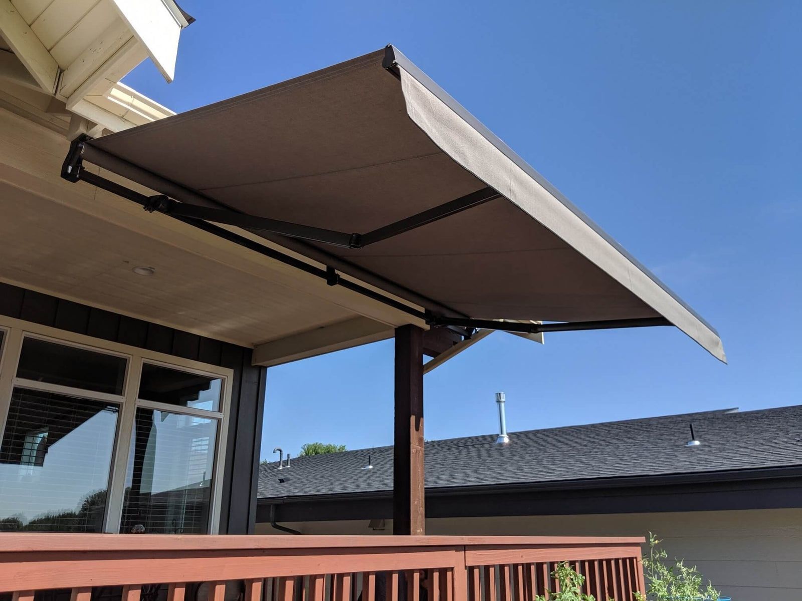Brown retractable awning extended over a patio beside a house, with blue sky above.