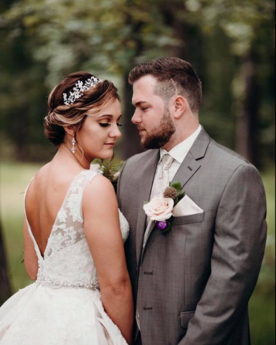 Bride and groom in wedding attire, standing close together outdoors with a soft blurred background.