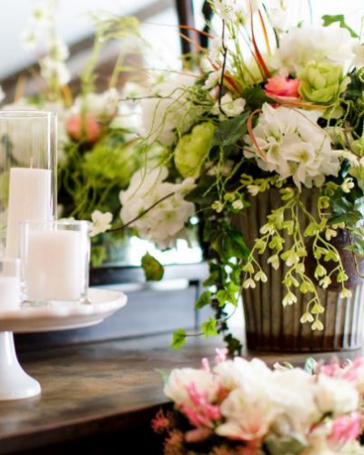 White candles beside lush green-and-white floral arrangements on a rustic table