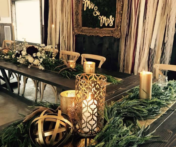 Decorated banquet table with candles, greenery, and rustic gold lanterns in a warm indoor setting