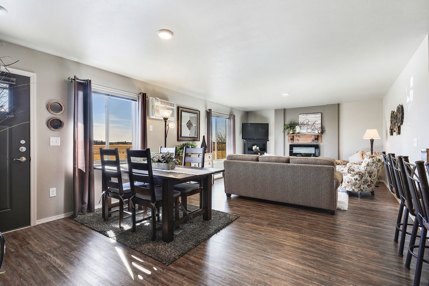 Bright living room with gray sectional, TV, wooden floor, coffee table, and large window seating area