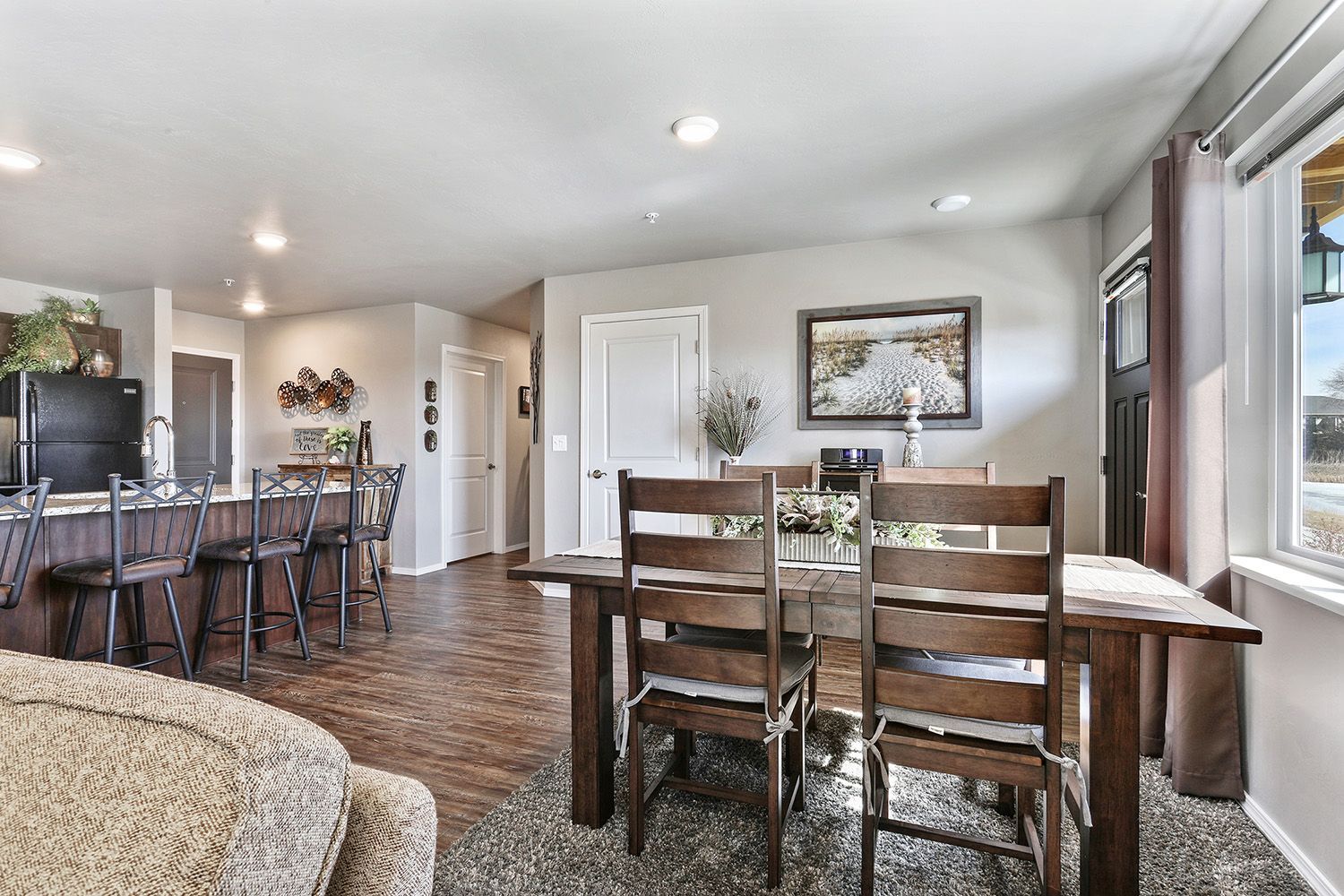 Open dining and living area with wood floors, dark dining table, bar stools, and large windows