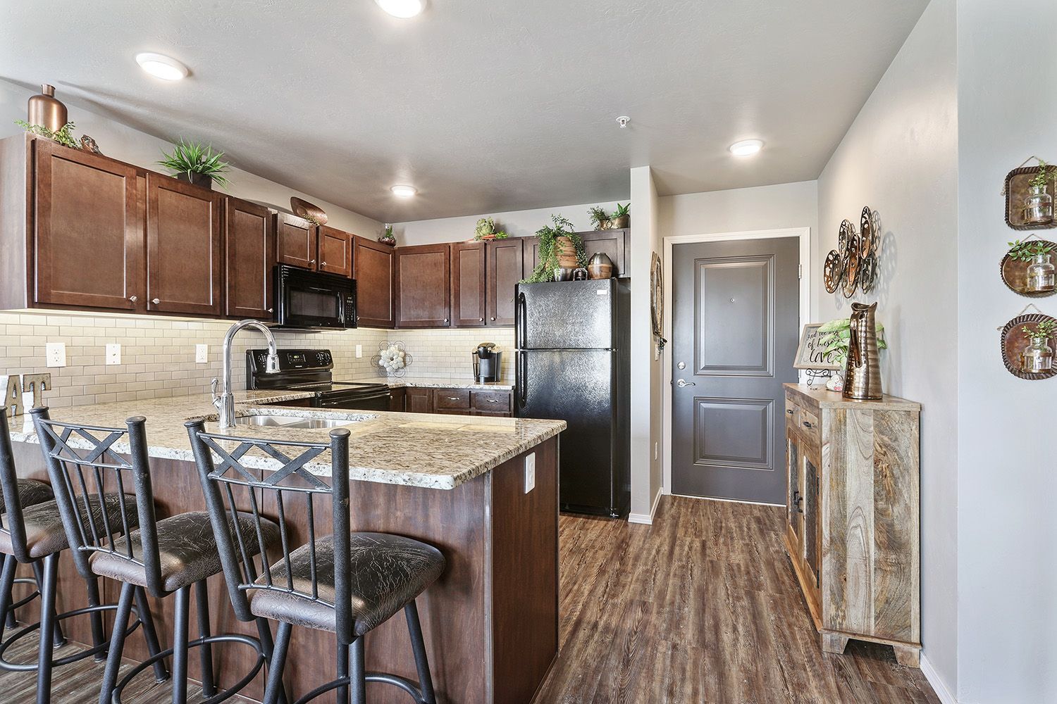 Modern kitchen with dark wood cabinets, granite island, bar stools, and a gray door