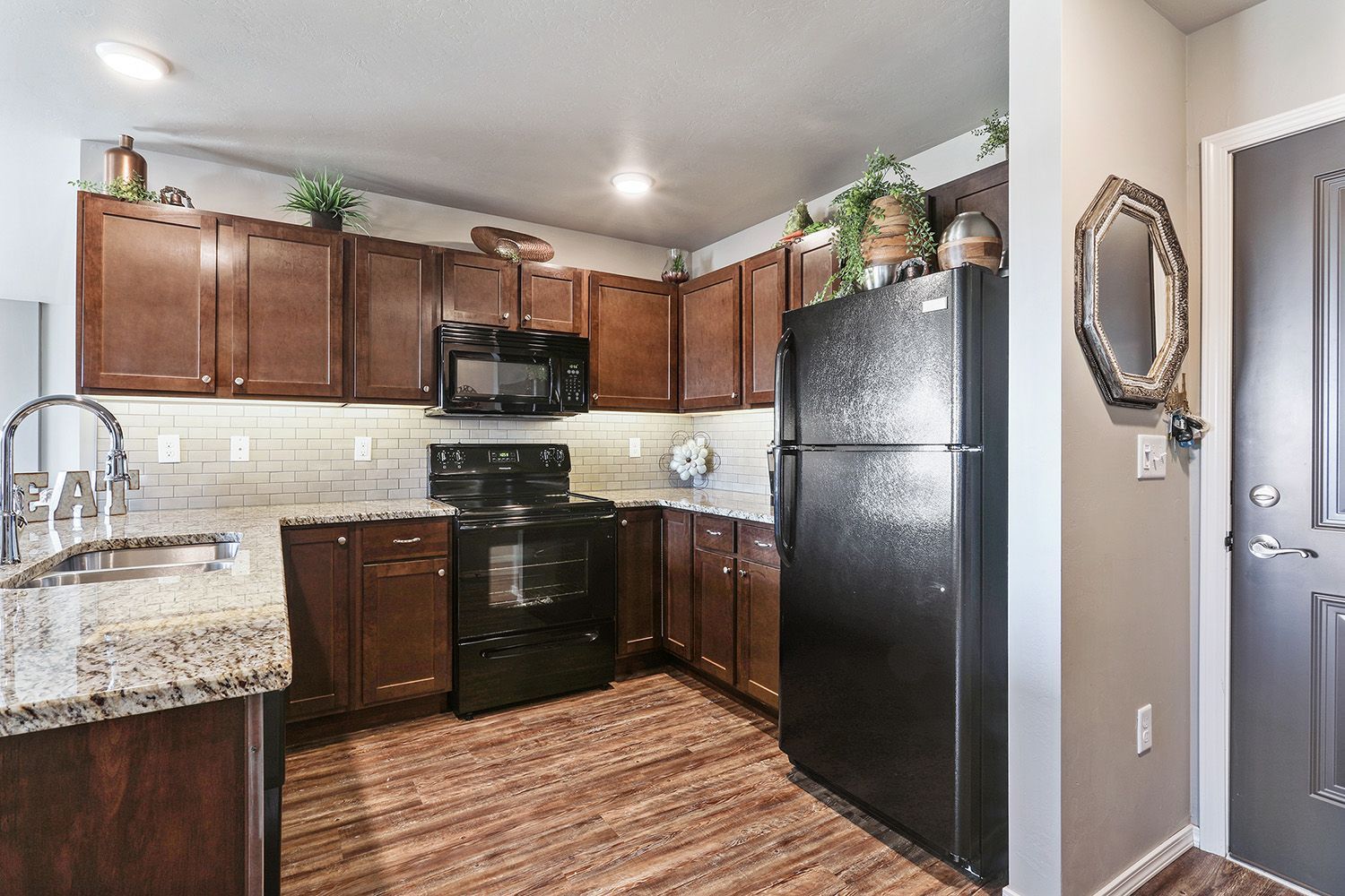 Compact modern kitchen with black appliances, wood cabinets, granite counters, and wood-look flooring.