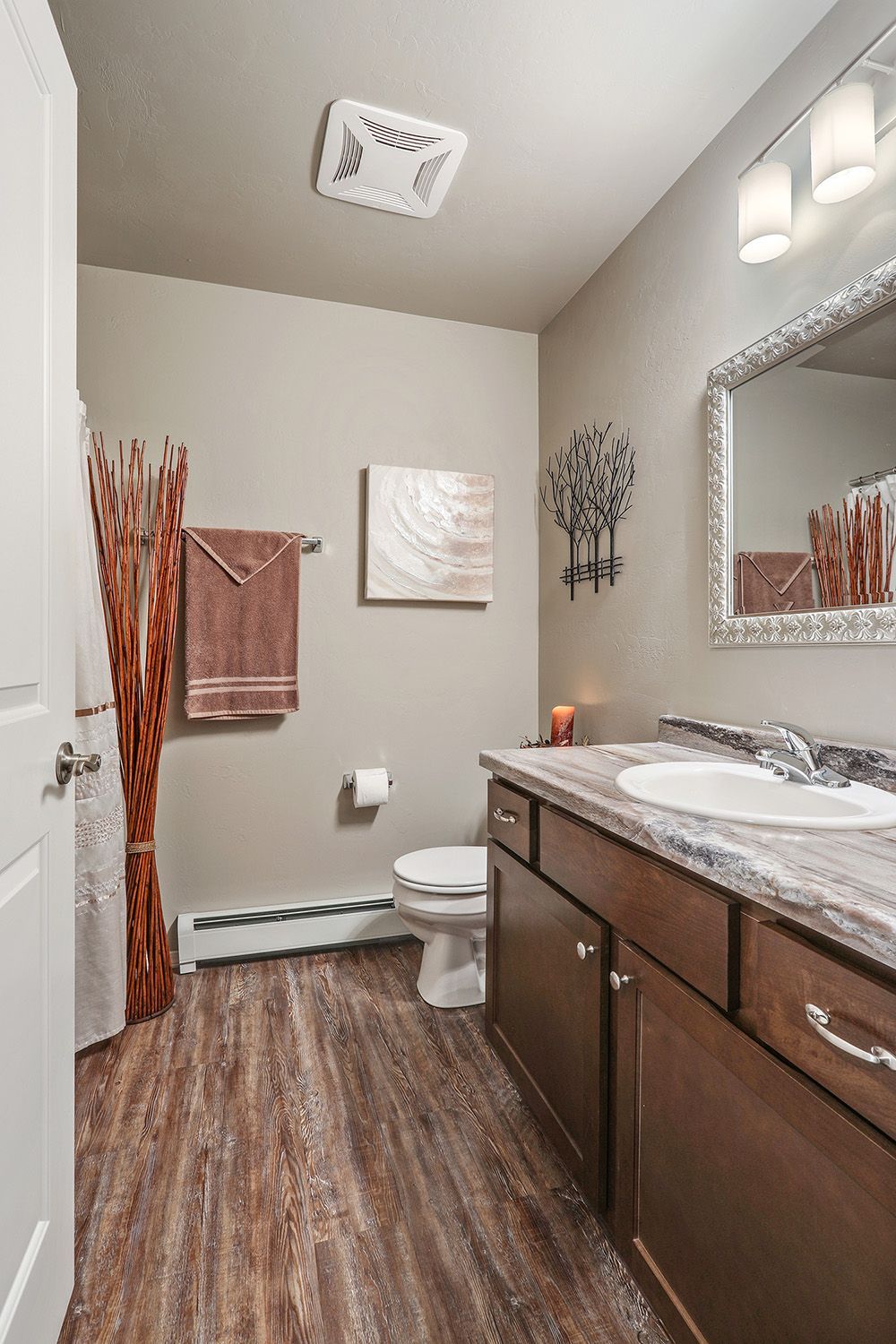 Modern bathroom with brown vanity, toilet, wood floor, wall art, and a window.