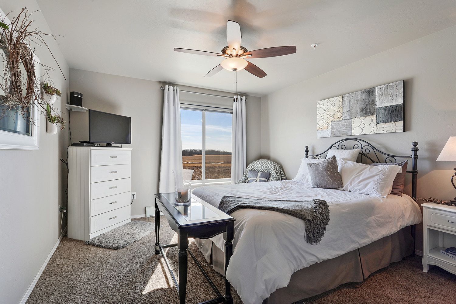 Bright bedroom with a bed, dresser, ceiling fan, and window view of snowy fields