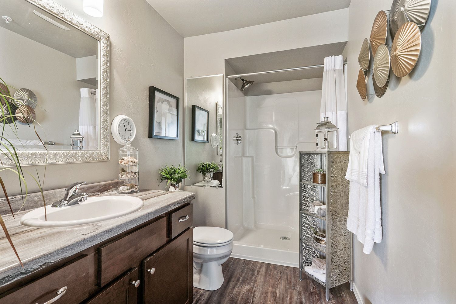 Small bathroom with dark vanity, white shower, wall mirror, and decorative accents.