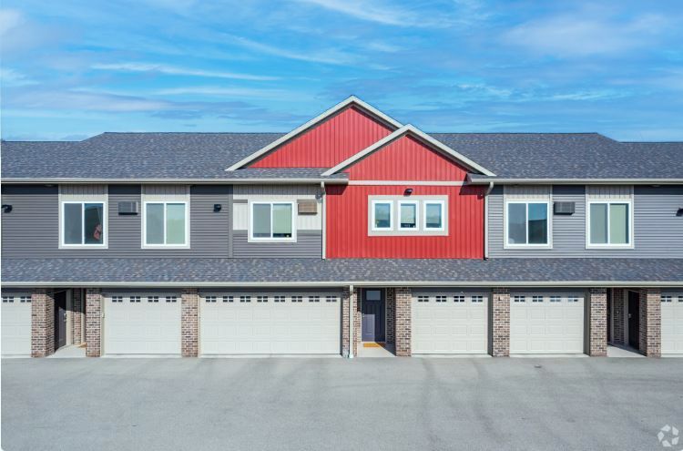 Row of modern townhouses with gray roofs, red center facade, and white garage doors under a blue sky