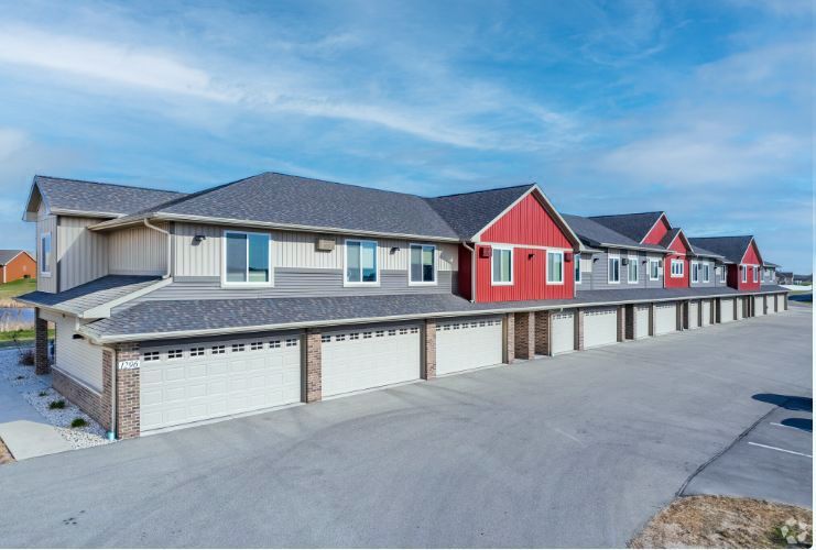 Row of modern townhouse garages with gray and red siding under a blue sky