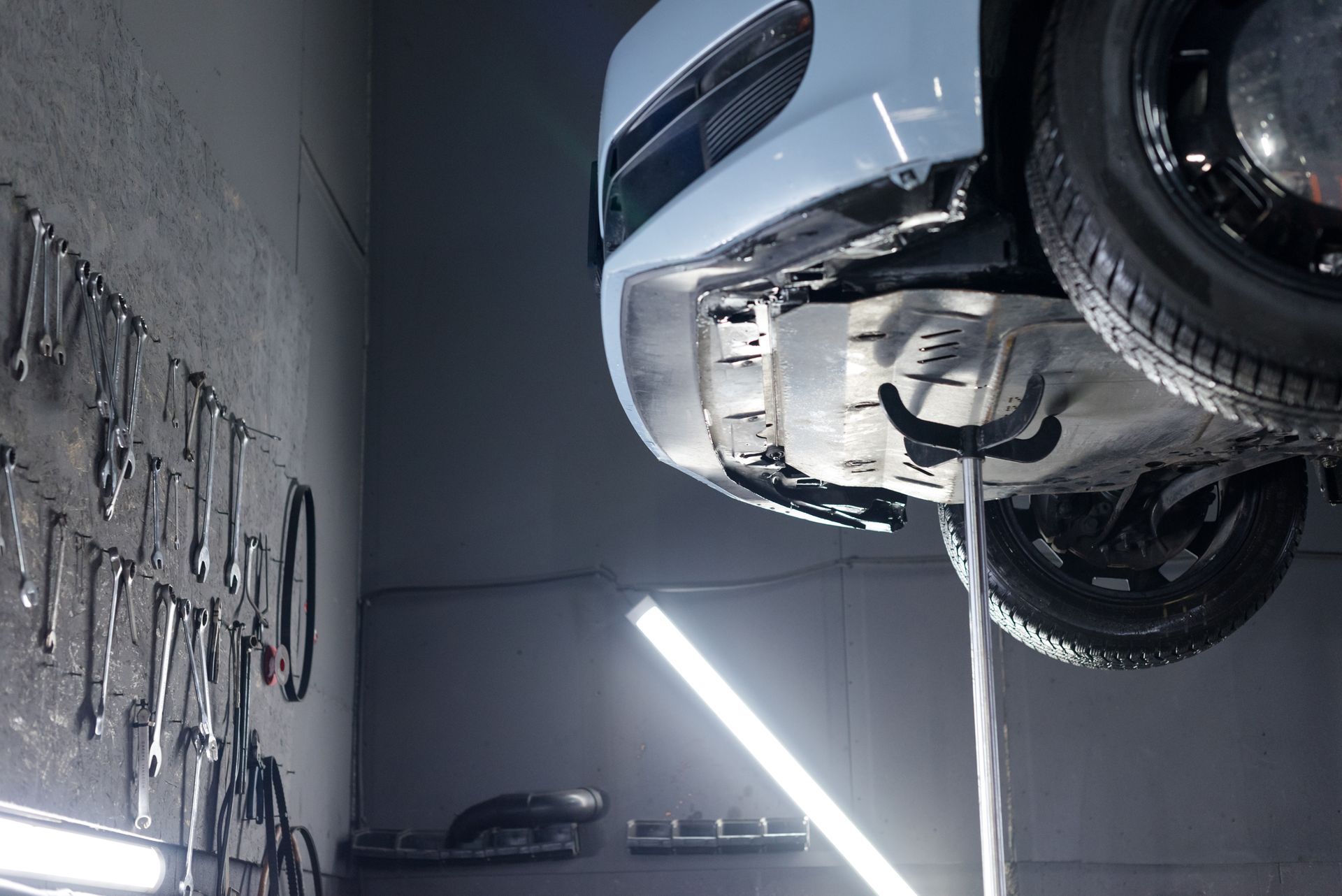 Car on a lift in a garage. Tools hang on the wall. A bright light shines beneath the vehicle. Car on a lift in a garage. Tools hang on the wall. A bright light shines beneath the vehicle.