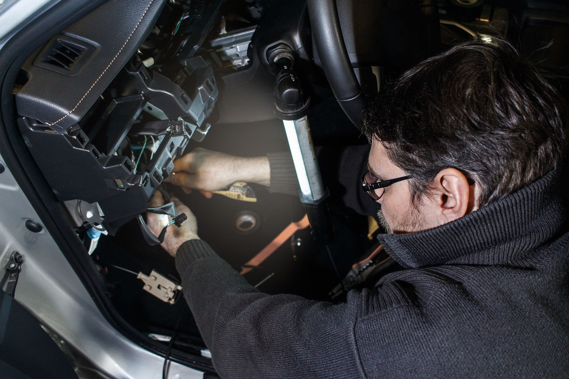 Mechanic working on a car's dashboard with a flashlight.