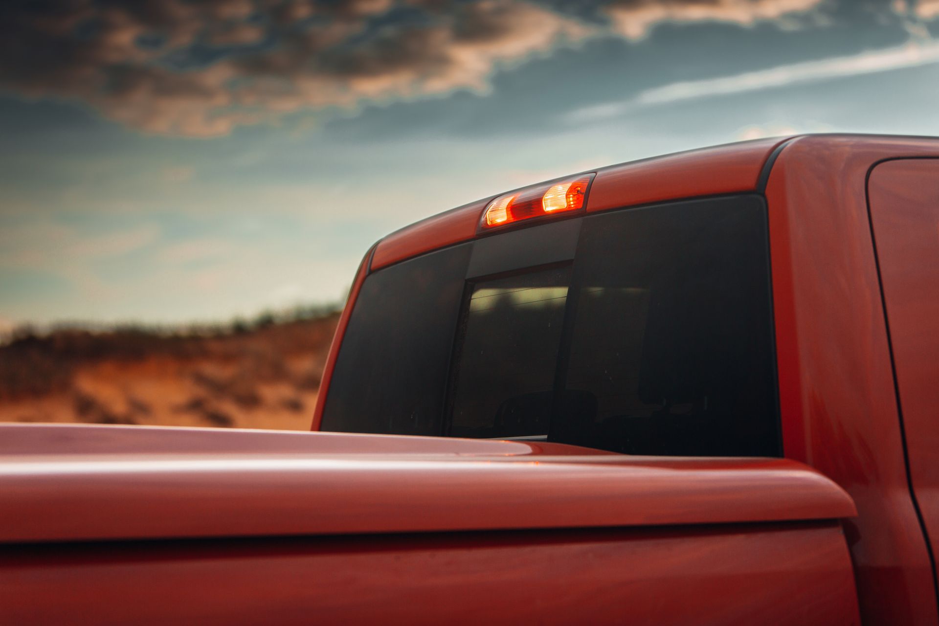 Red pickup truck bed and rear cab with a lit brake light against a desert landscape. Red pickup truck bed and rear cab with a lit brake light against a desert landscape.