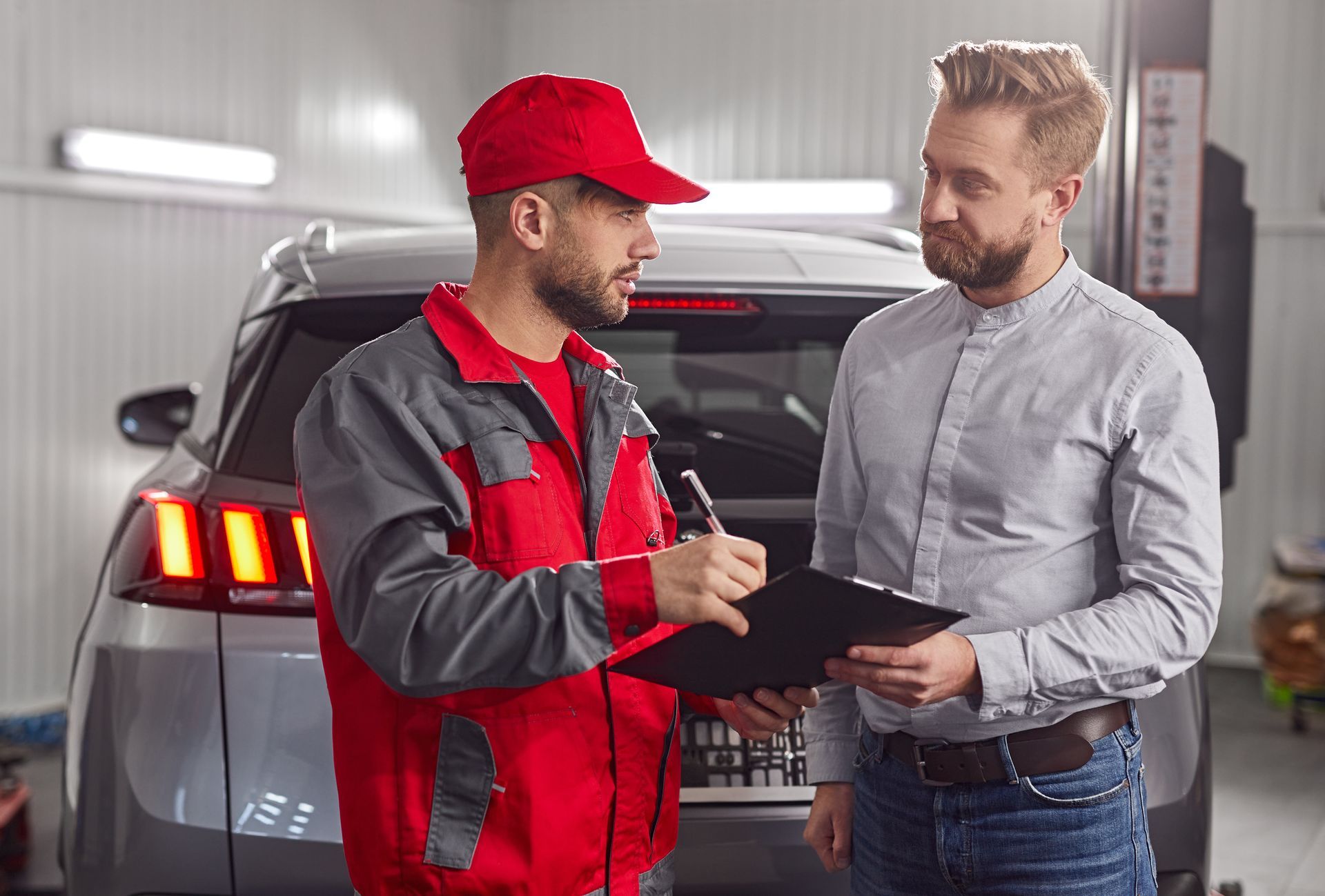 Mechanic in red overalls explains repairs to a customer in a car repair shop. Mechanic in red overalls explains repairs to a customer in a car repair shop.