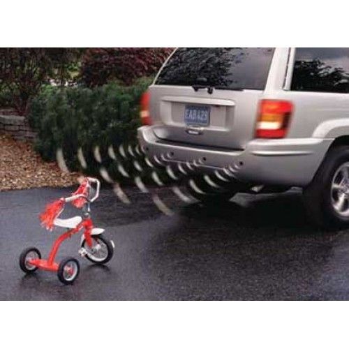 SUV backing up, sensors activated near red tricycle on driveway.