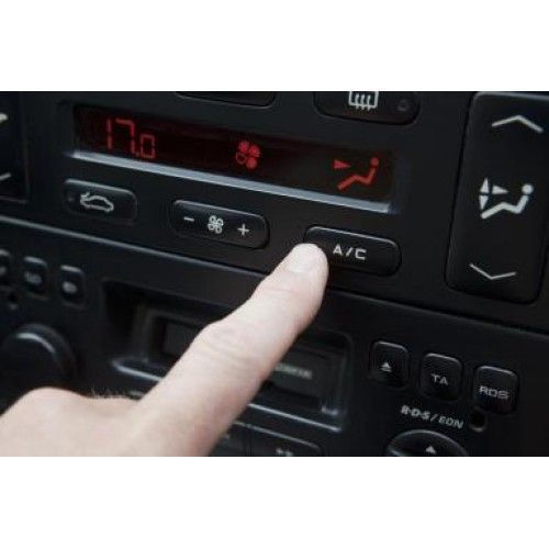 A hand pressing an A/C button on a car's dashboard. A display shows 17.0 and a fan symbol.