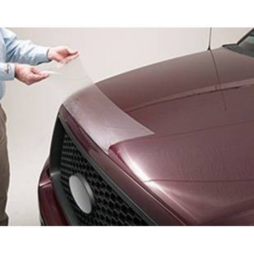 Person applying a clear protective film to the hood of a red car.