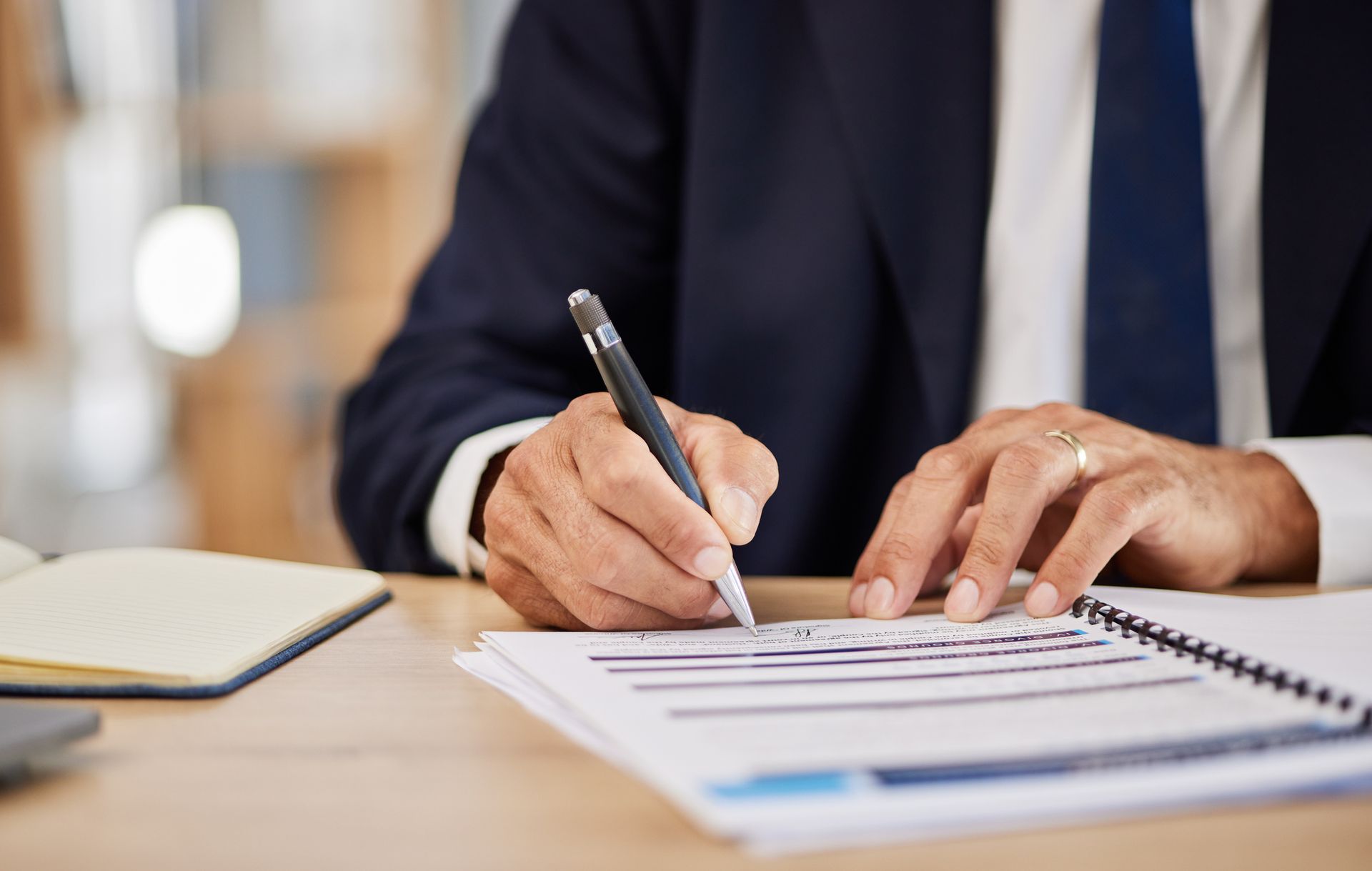 A man in a suit and tie is writing on a piece of paper with a pen.