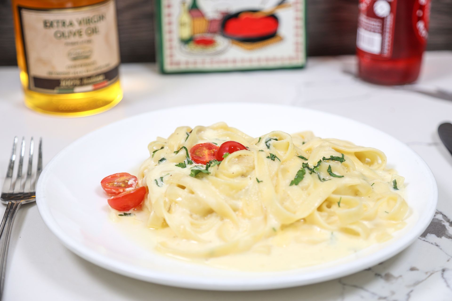 Plate of creamy pasta with cherry tomatoes and herbs on a white table, with wine and condiments in the background