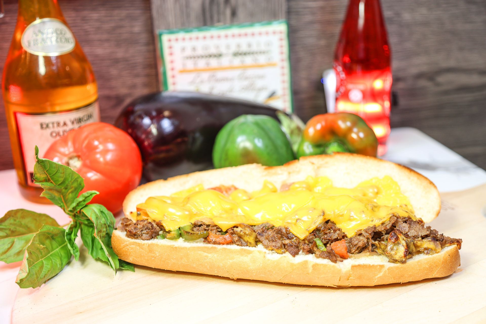 Cheesy meat sandwich on a table with tomatoes, peppers, and bottles in the background