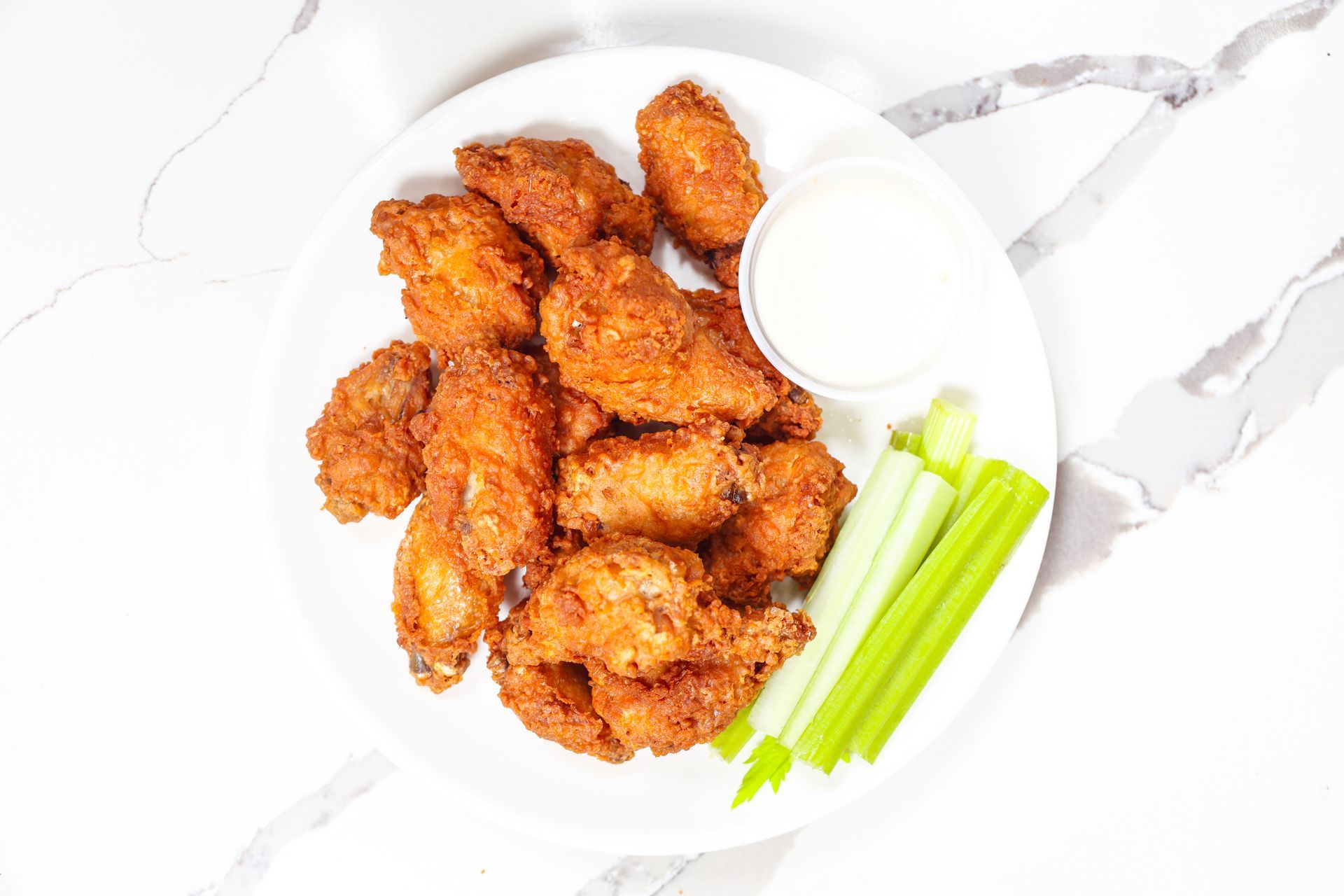 Fried chicken wings with celery sticks and dipping sauce on a white plate