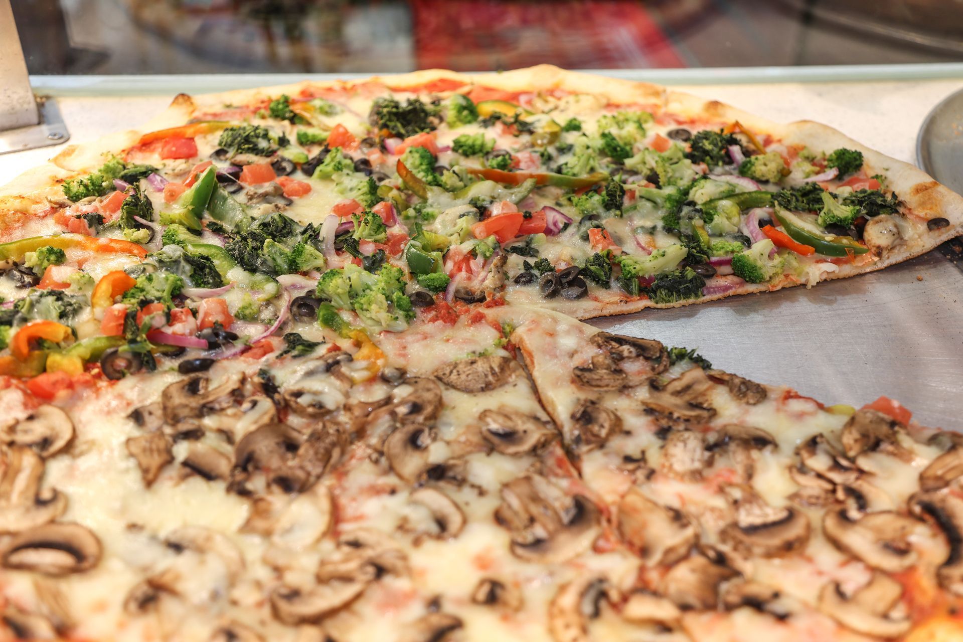 Slices of vegetable pizza with mushrooms, tomatoes, and greens on a display tray