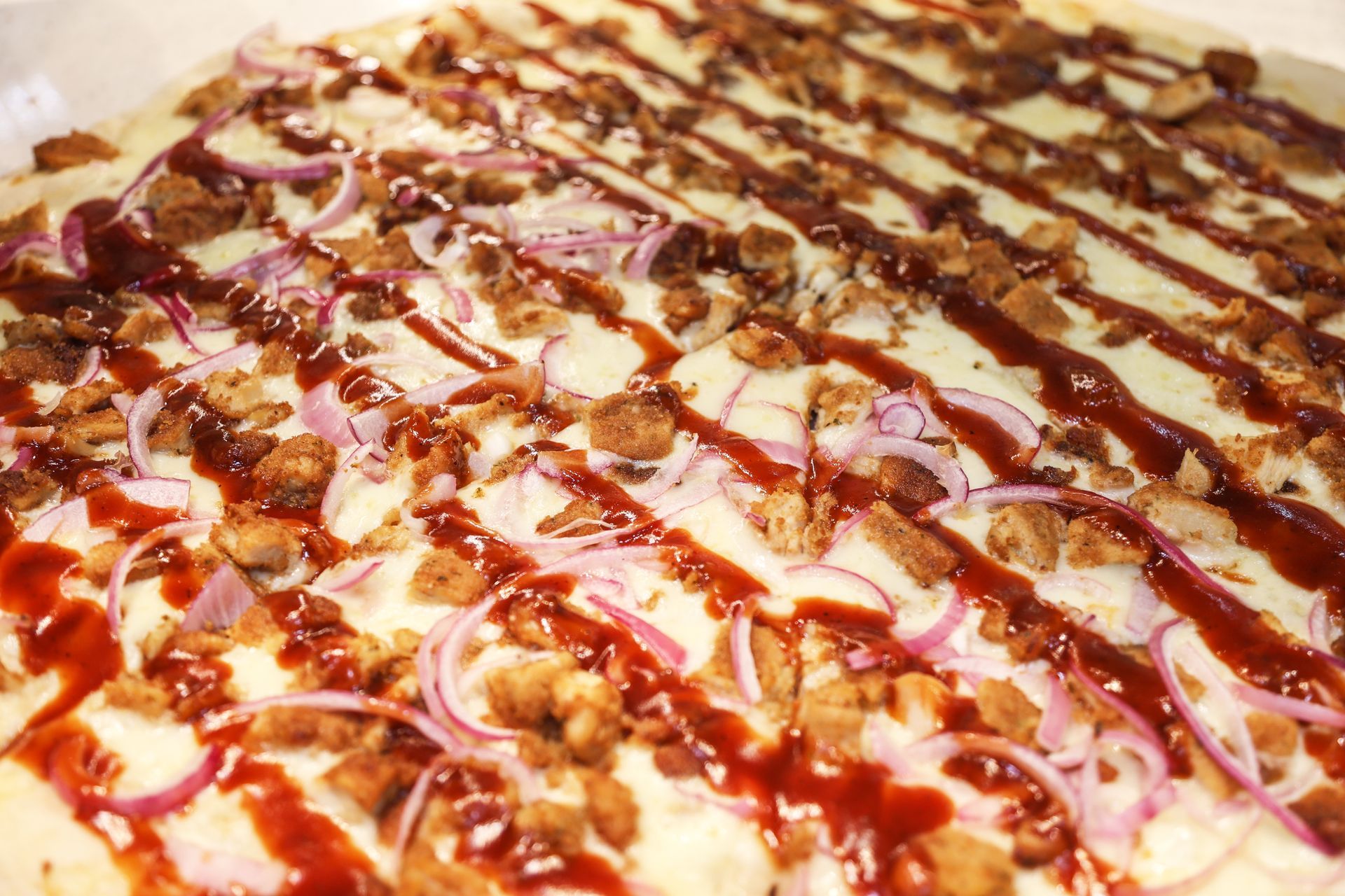 Close-up of a pizza topped with cheese, onions, and drizzled sauce.