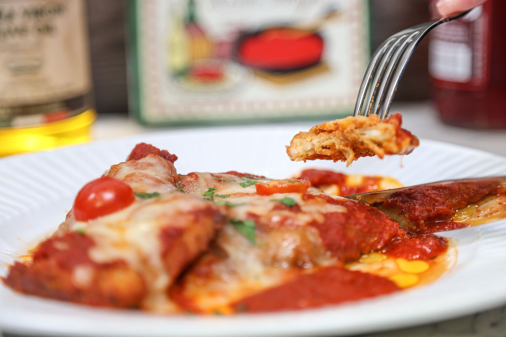 Fork lifting a cheesy slice of pizza on a white plate, with tomatoes and sauce on the side