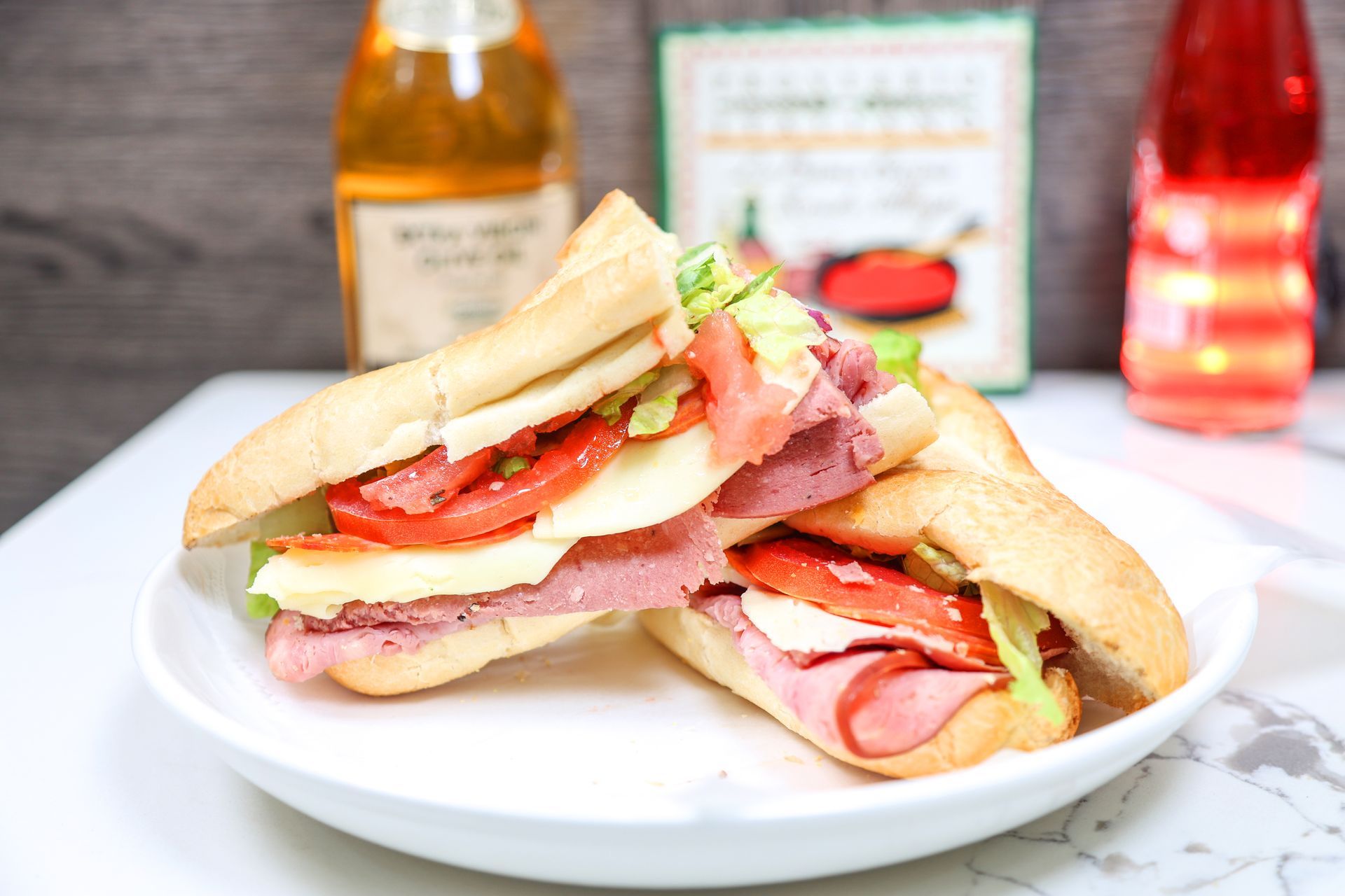 Sandwich with ham, cheese, tomato, and lettuce on a white plate, with condiments in the background