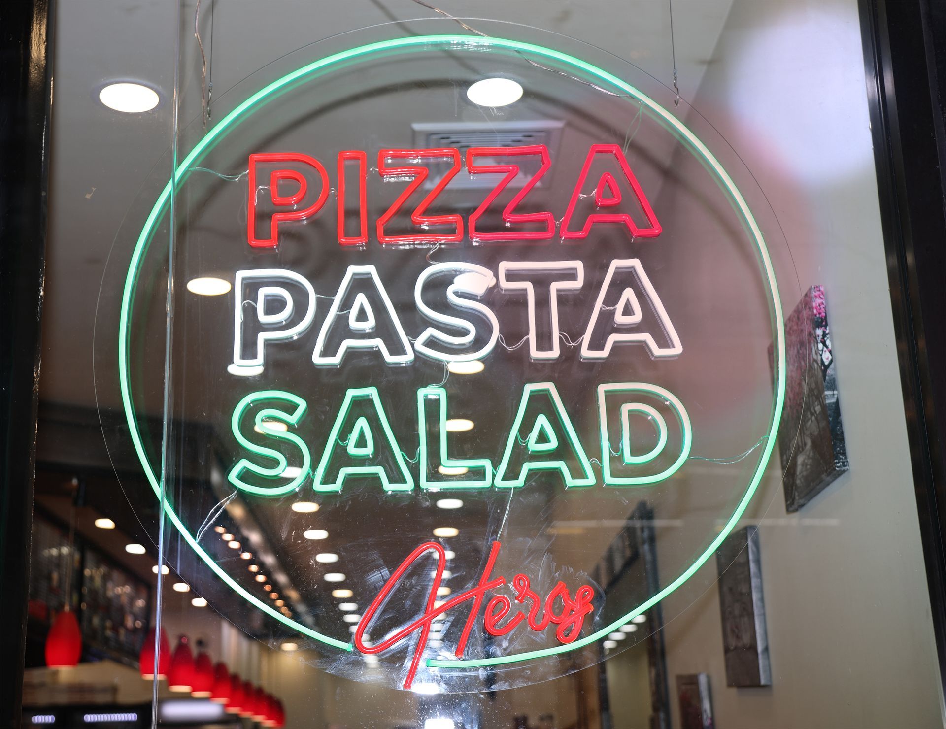 Neon restaurant sign reading “PIZZA PASTA SALAD,” with a glowing circular outline