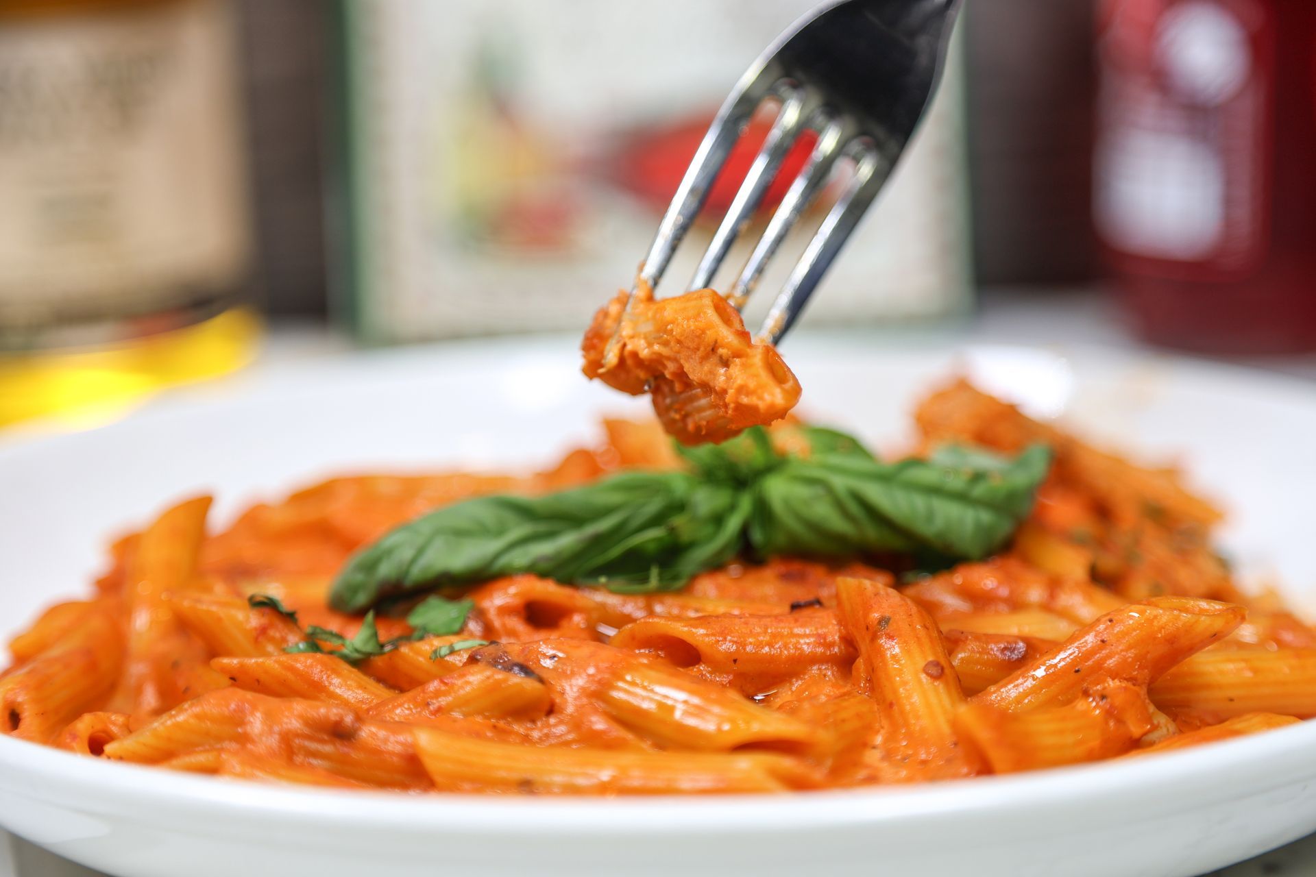 Fork lifting penne pasta with tomato sauce and basil on a white plate