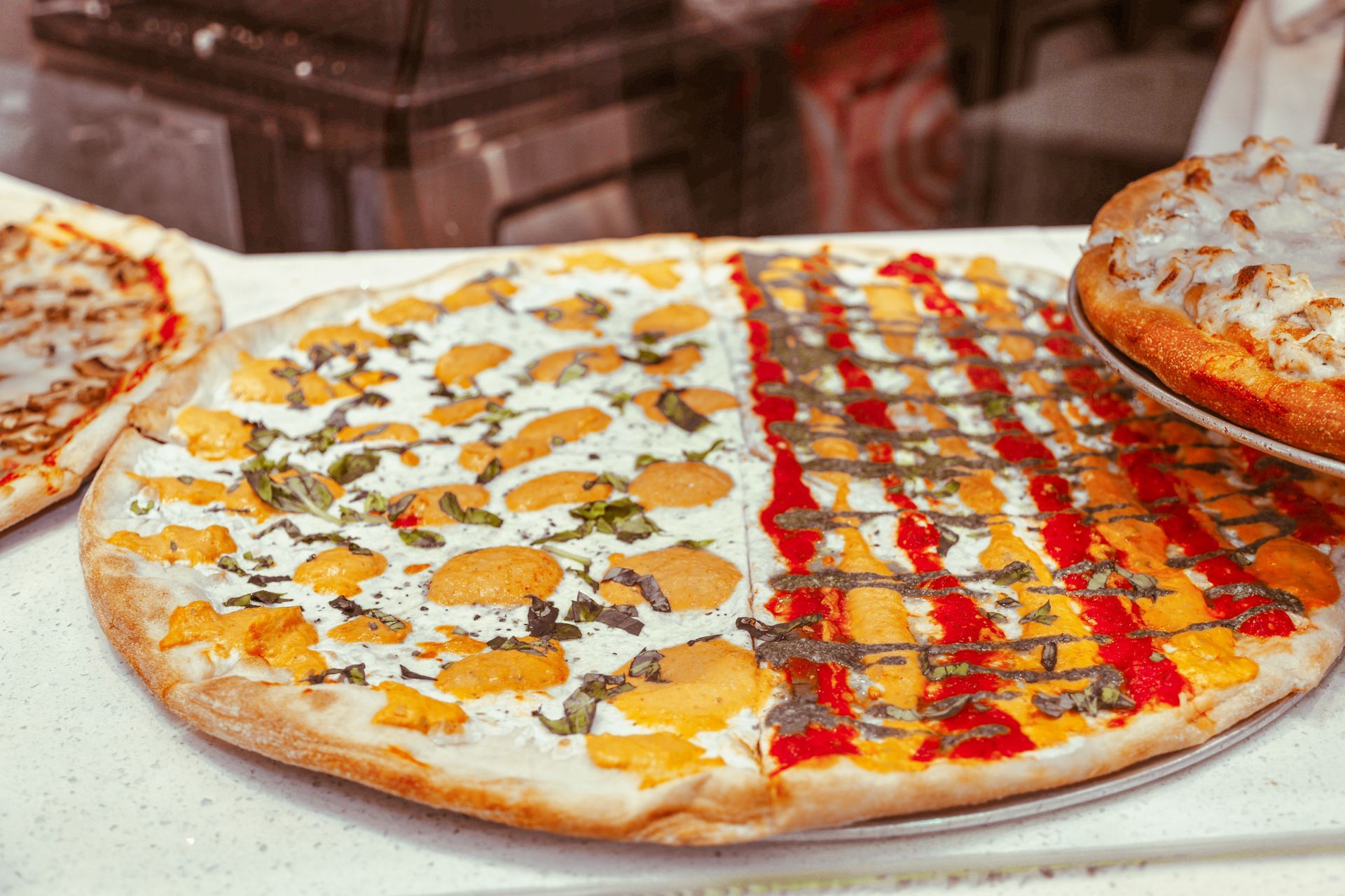 A large pizza split into three topping styles on a serving tray, including cheese, drizzled sauce, and bacon