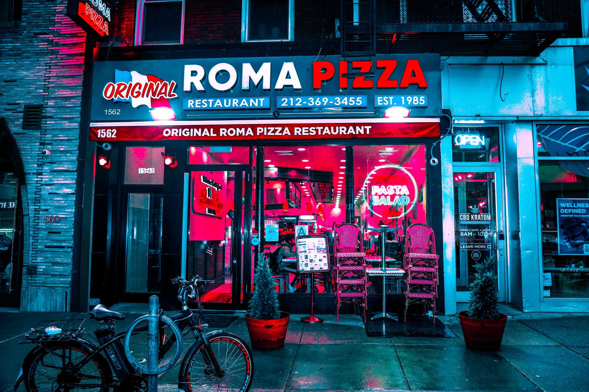 Neon-lit Roma Pizza restaurant storefront at night with red signage and outdoor seating