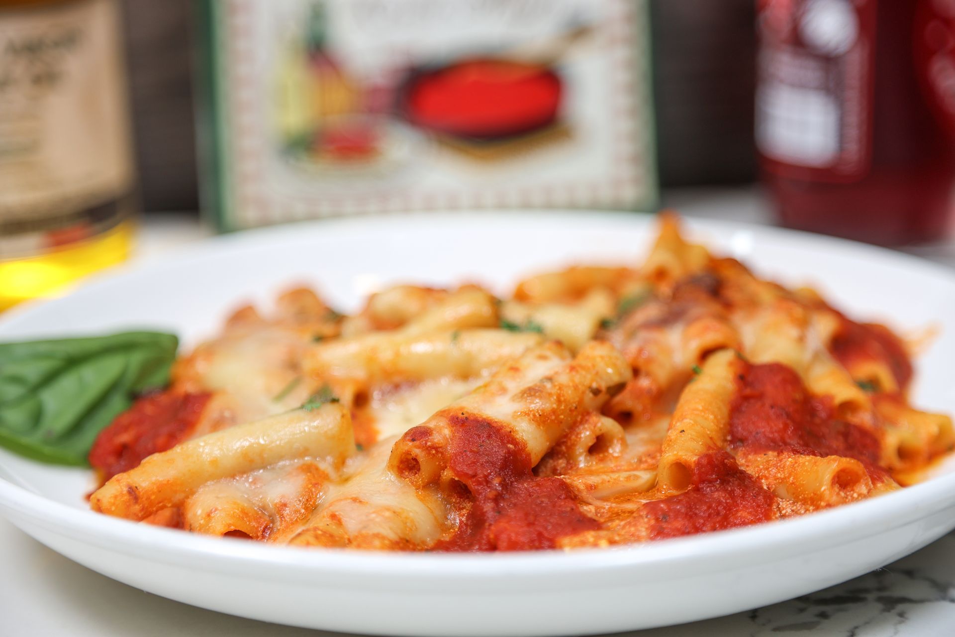 Plate of penne pasta in tomato sauce with melted cheese, garnished with basil leaves