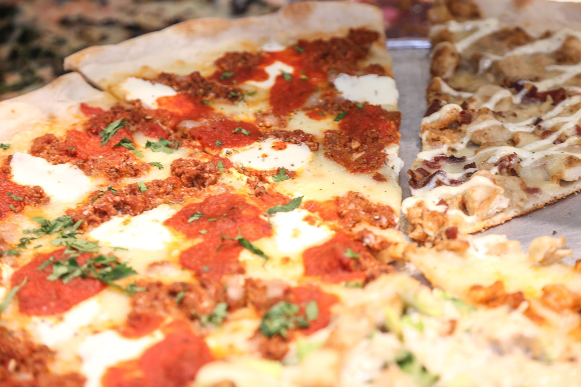 Close-up of a pizza with tomato sauce, melted cheese, herbs, and sliced toppings on a tray