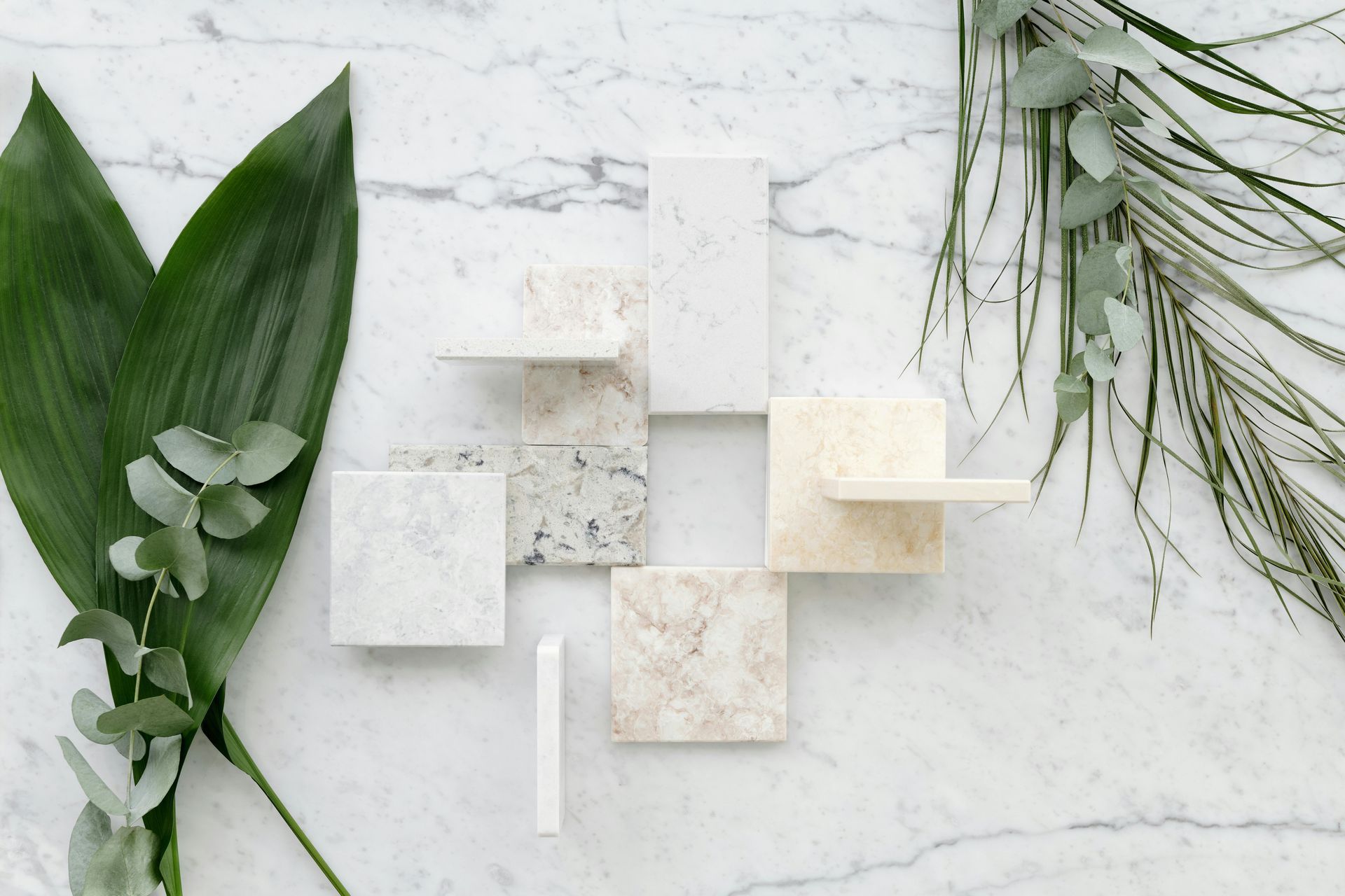 Marble tiles and greenery arranged on a white marble surface.