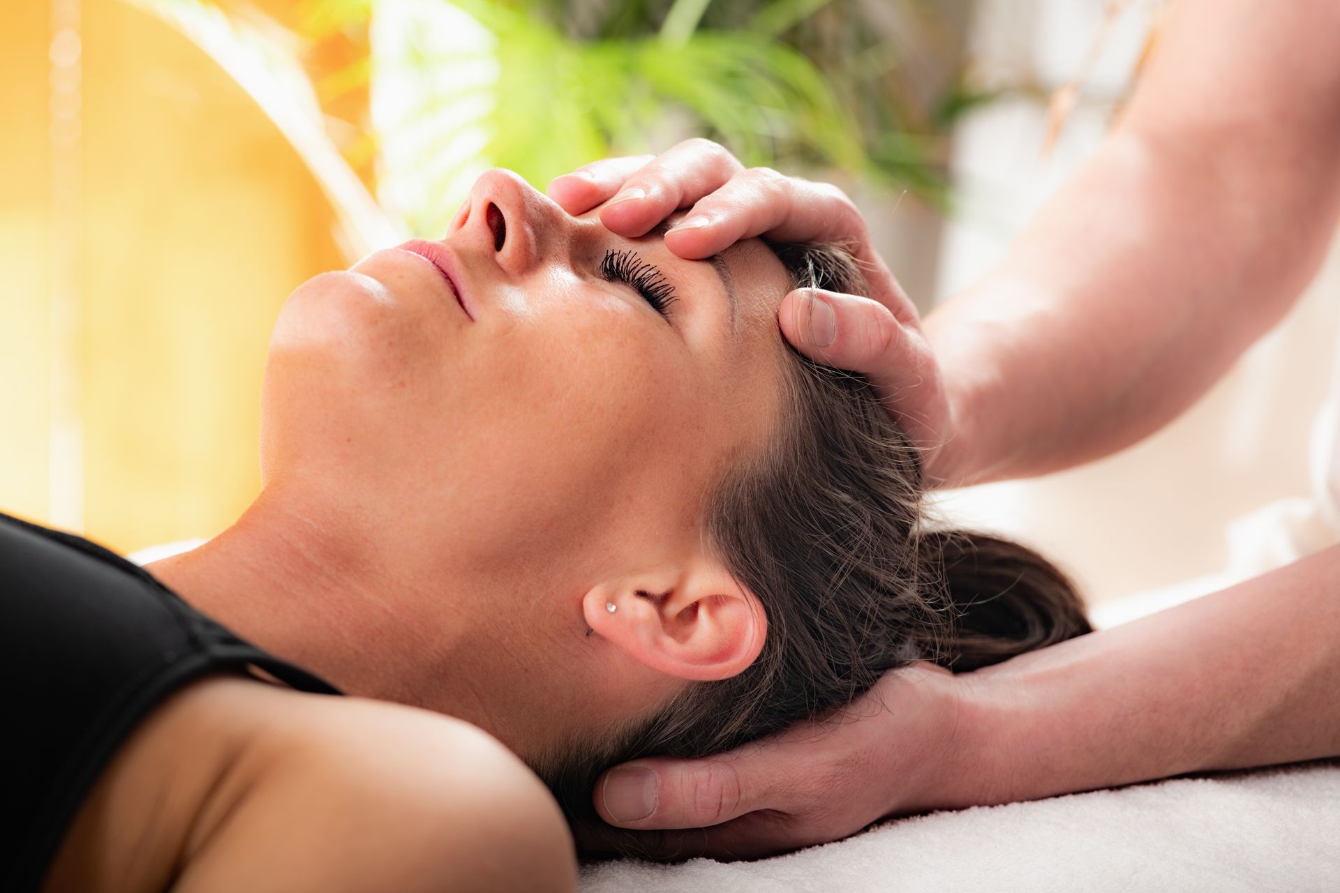A person receives a gentle head massage from a practitioner, who holds the person's forehead and base of the skull.