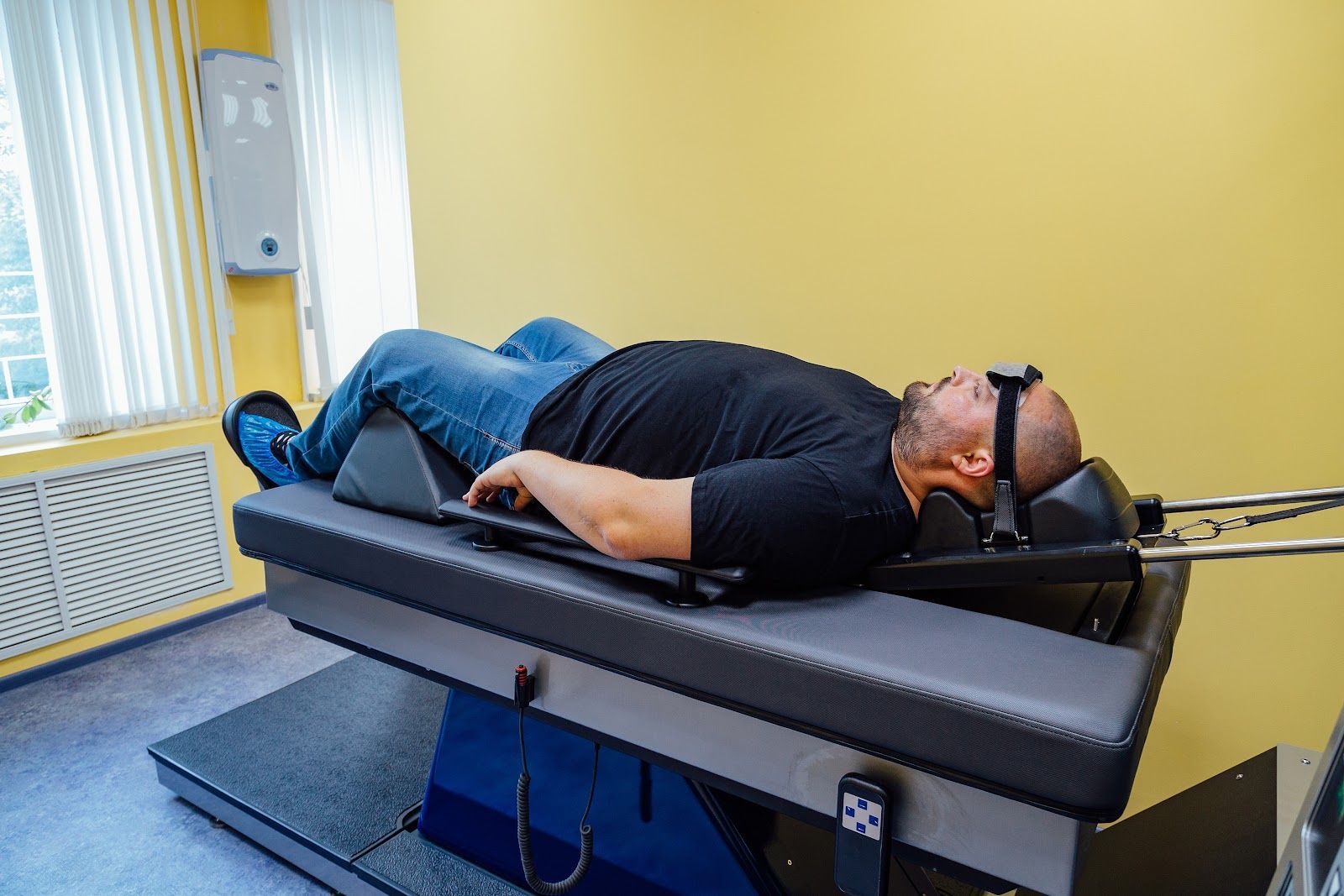 Person lying on a padded treatment table in a clinic, wearing sunglasses, with a yellow wall in the background