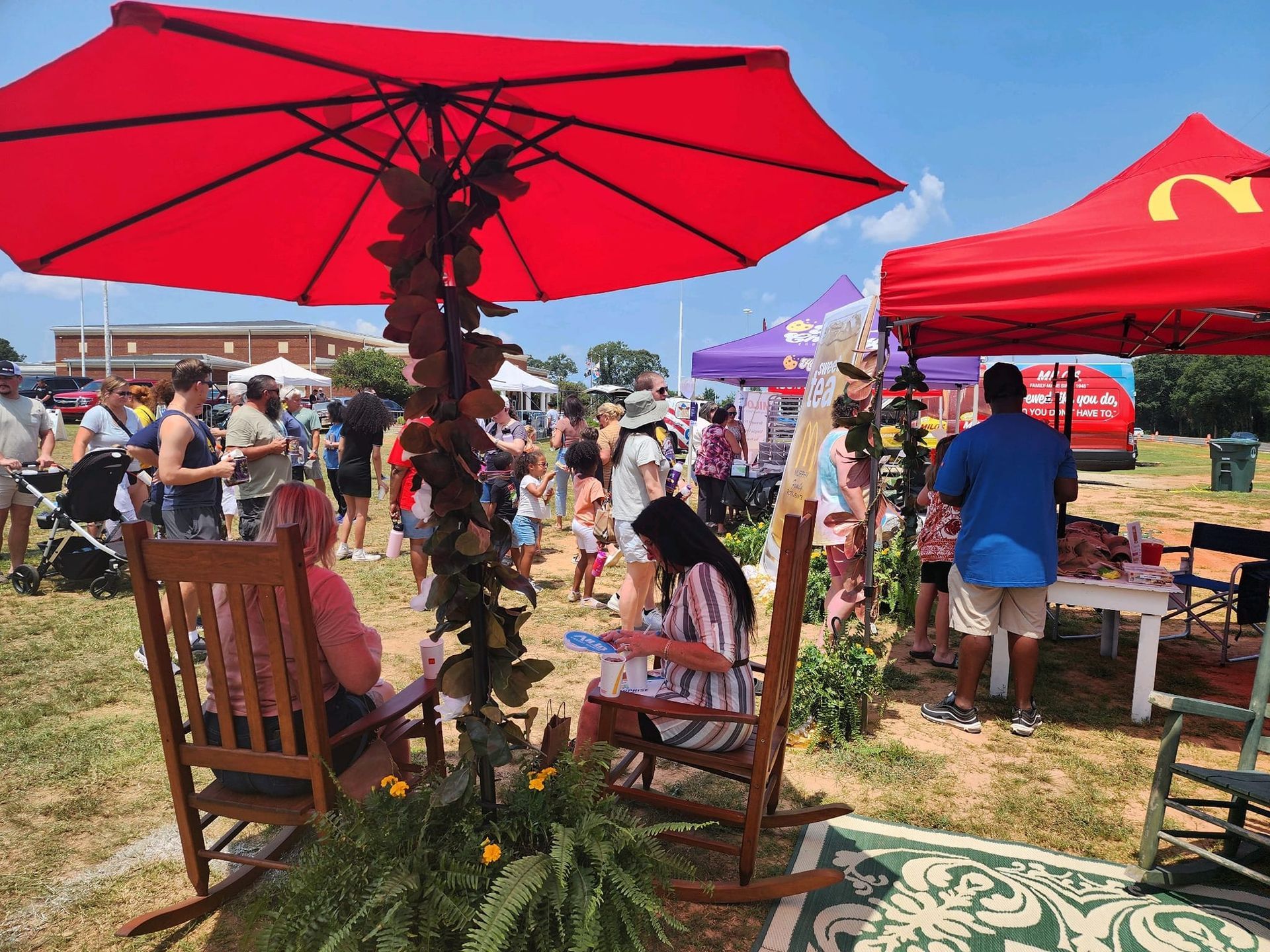 A woman is sitting in a rocking chair under an umbrella at a festival.