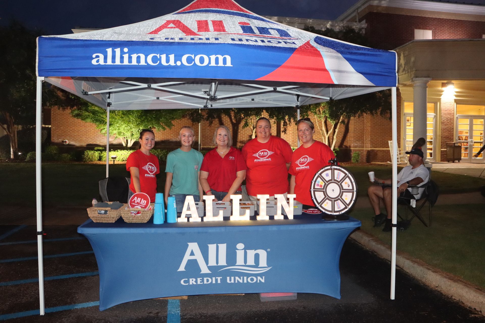 A group of people standing under an all in credit union tent