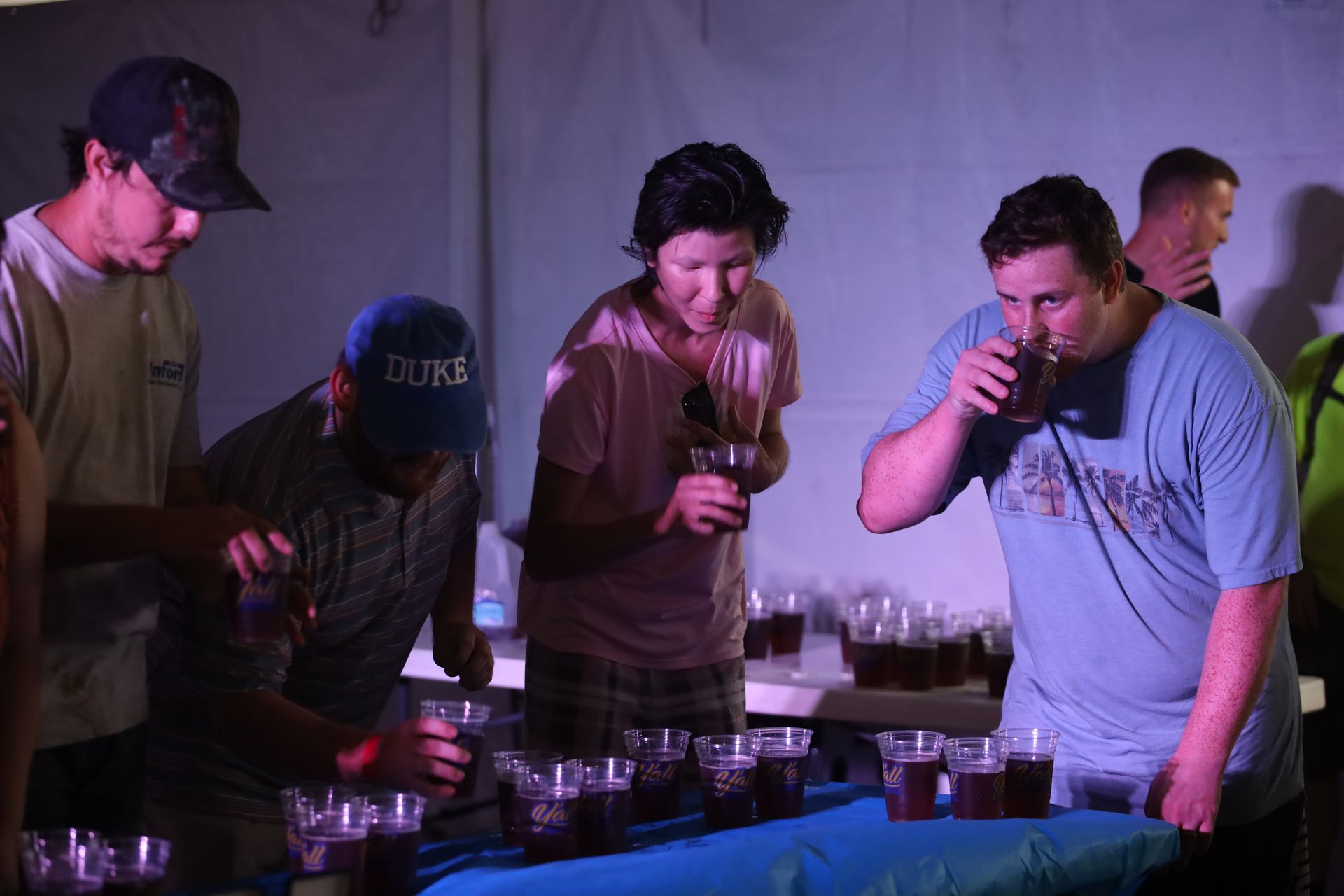 A group of people are standing around a table drinking beer.