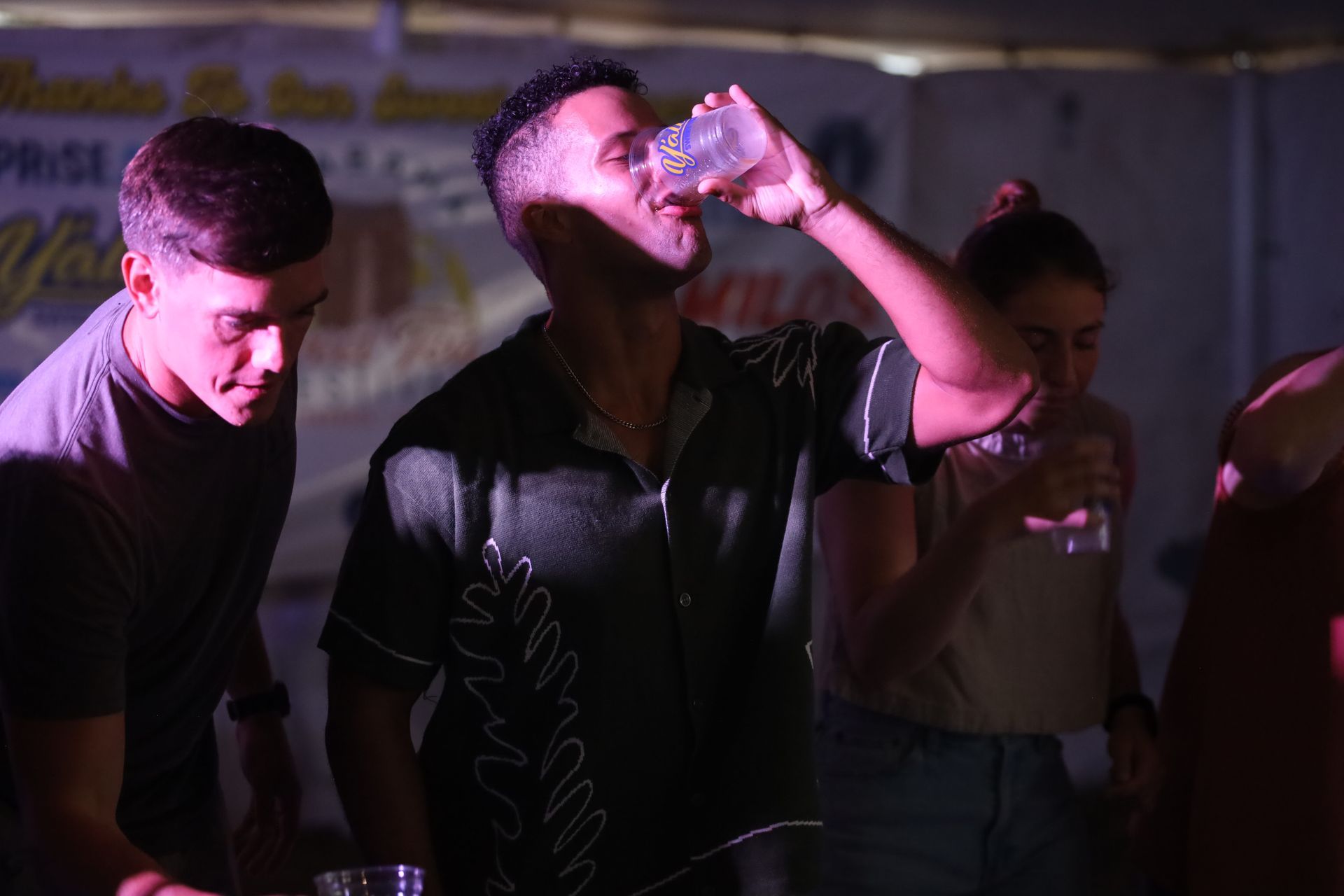 A man is drinking water from a bottle in a dark room.