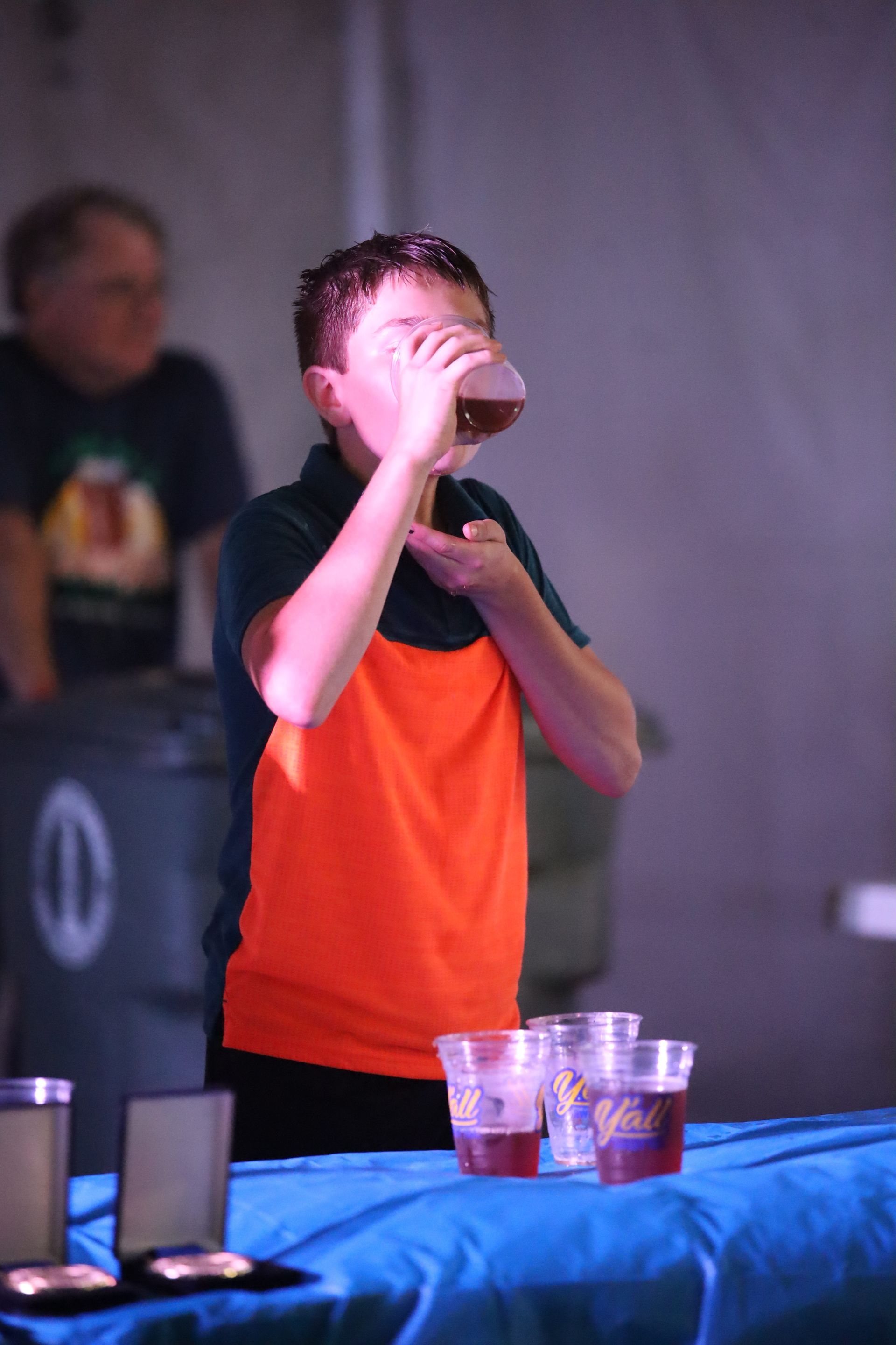 A young boy is drinking a beer from a plastic cup