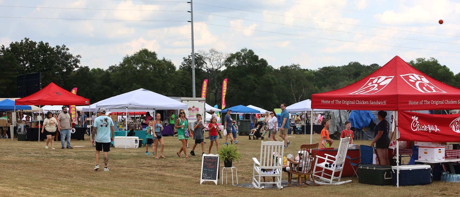 A group of people are standing in a field with tents and rocking chairs.