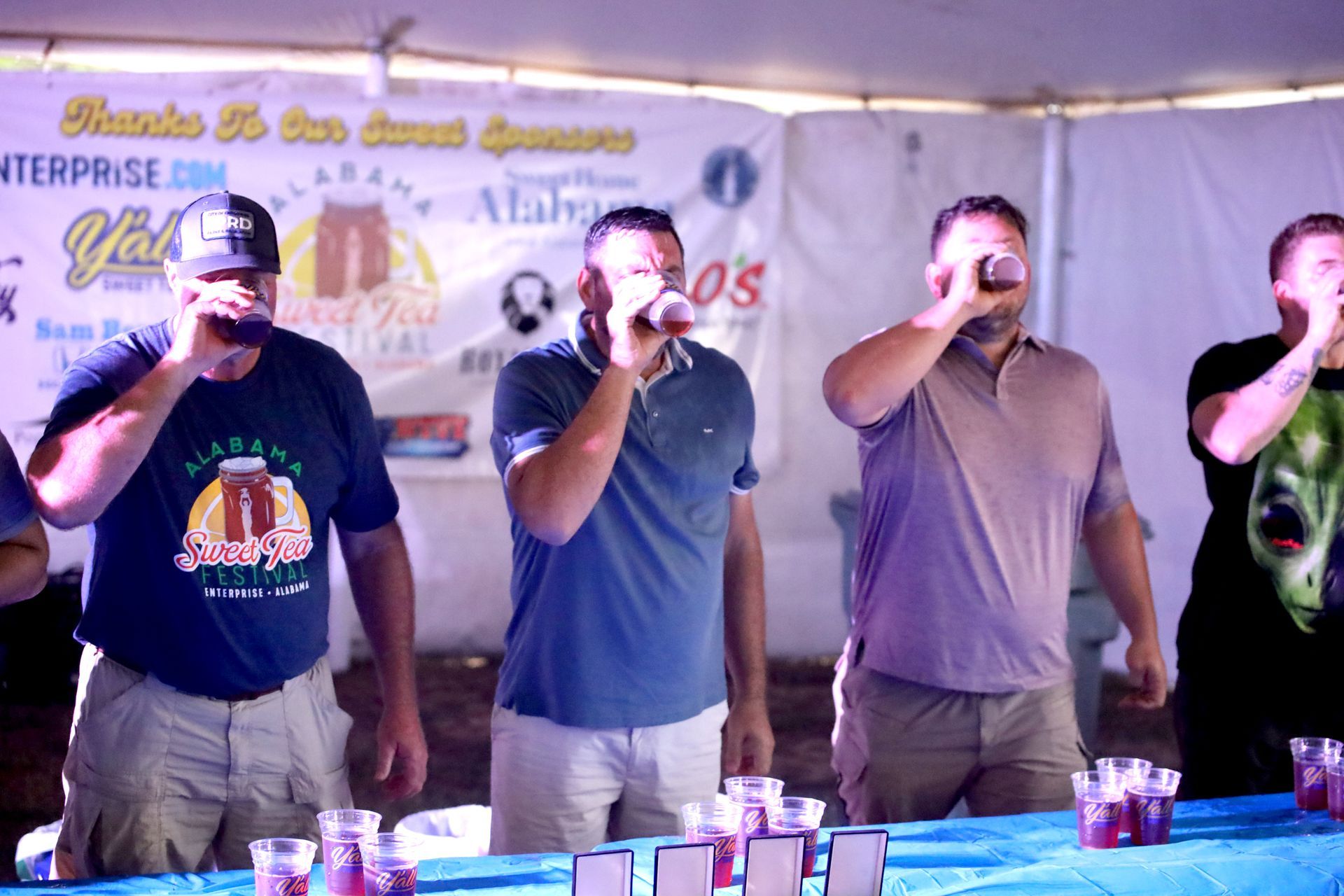 A group of men are standing around a table drinking beer